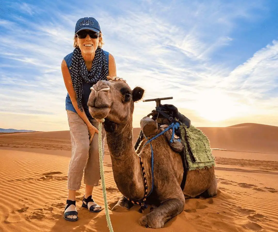 Happy traveler with a camel during a sunset camel trek in the Merzouga Sahara Desert, Morocco.