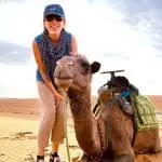 Happy traveler with a camel during a sunset camel trek in the Merzouga Sahara Desert, Morocco.